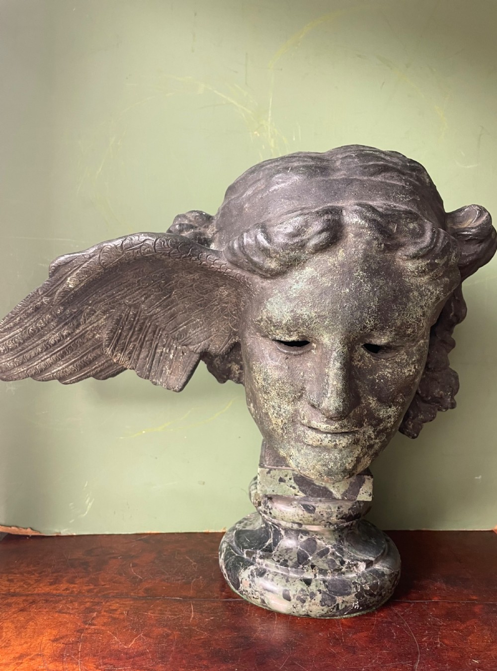 A 19th-century verdigris bronze head study of Hypnos featuring a winged temple, mounted on a round variegated green marble base. View XVII