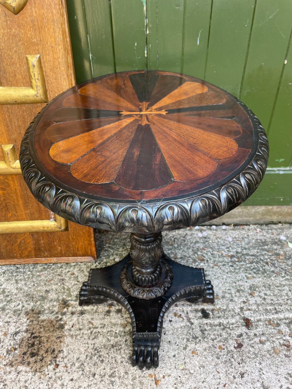 A 19th-century Anglo-Indian pedestal table featuring a carved ebony base and a starburst inlaid specimen wood top. View VII