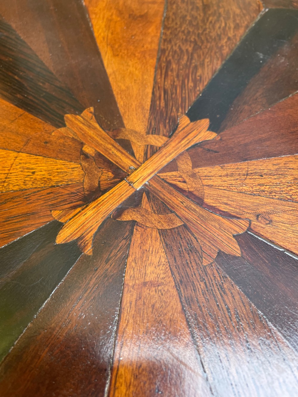 A 19th-century Anglo-Indian pedestal table featuring a carved ebony base and a starburst inlaid specimen wood top. View XIV