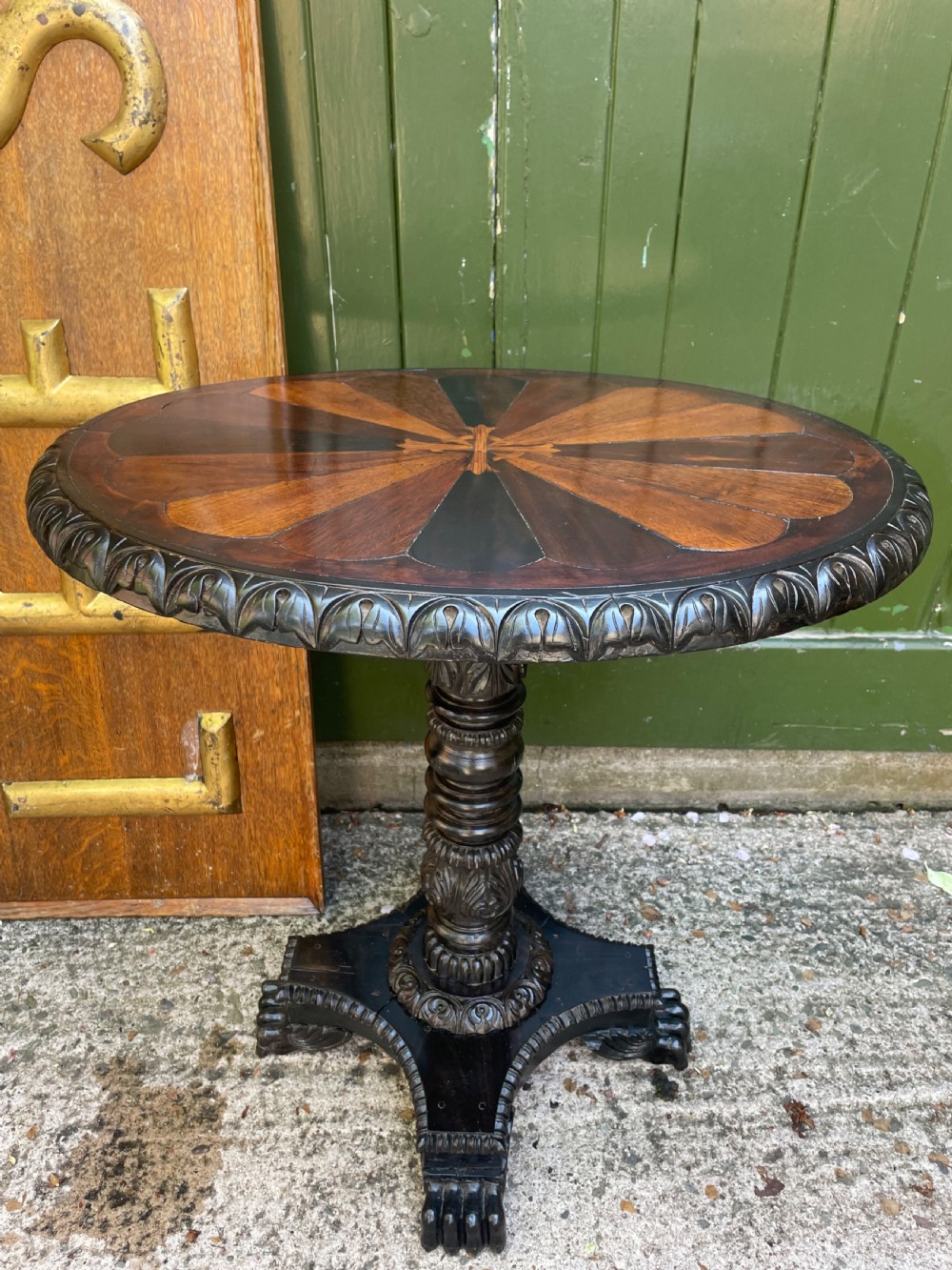 A 19th-century Anglo-Indian pedestal table featuring a carved ebony base and a starburst inlaid specimen wood top. View XV
