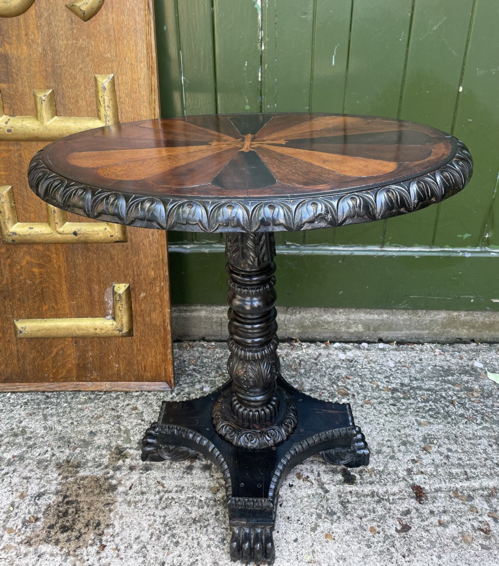 A 19th-century Anglo-Indian pedestal table featuring a carved ebony base and a starburst inlaid specimen wood top.