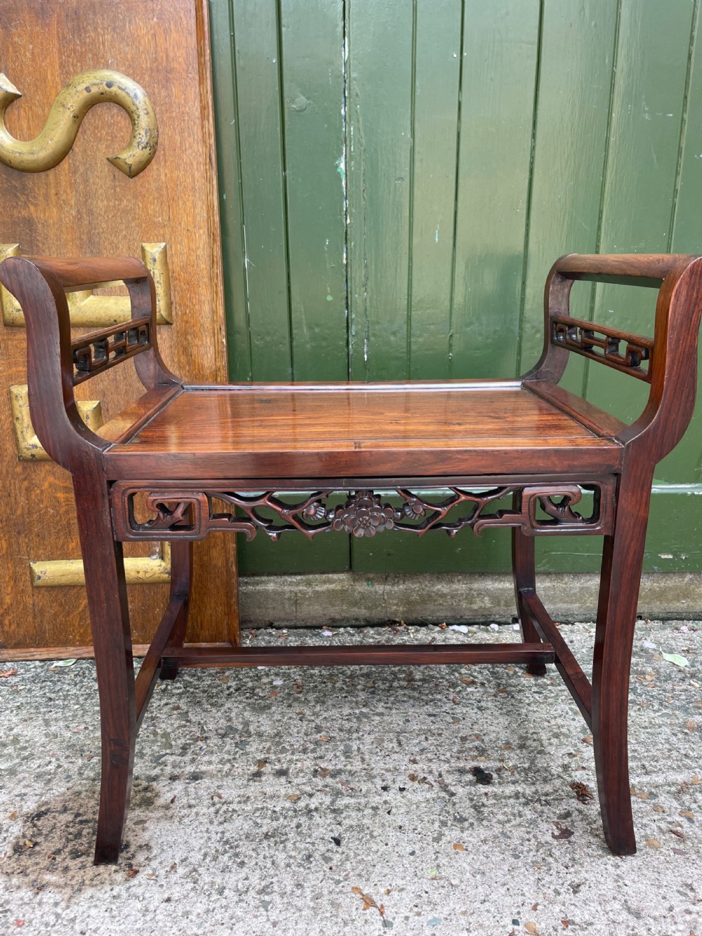A late Qing Dynasty Chinese carved hardwood dressing stool featuring raised handles, openwork carved aprons, and square legs with stretchers.