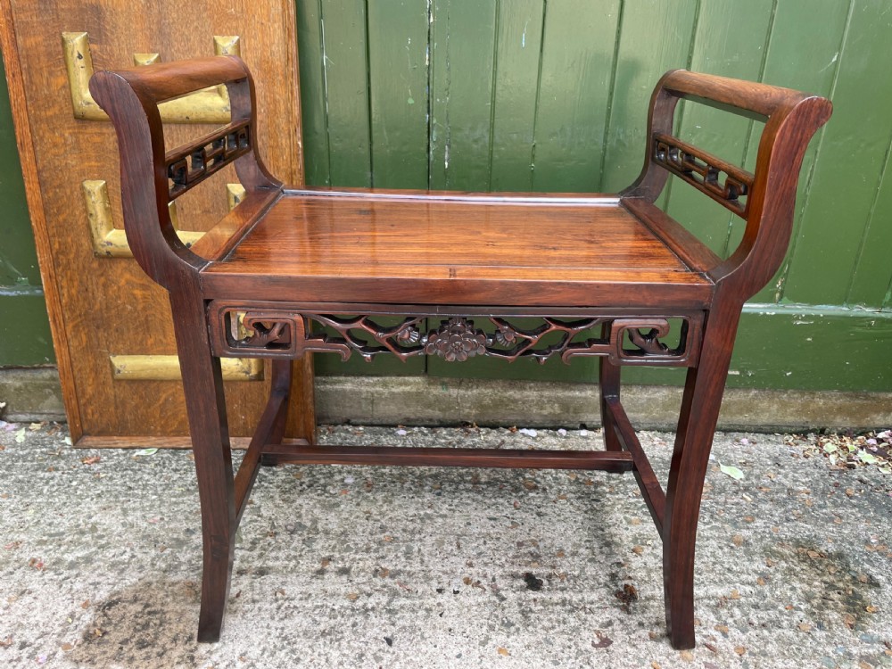 A late Qing Dynasty Chinese carved hardwood dressing stool featuring raised handles, openwork carved aprons, and square legs with stretchers. View XIV