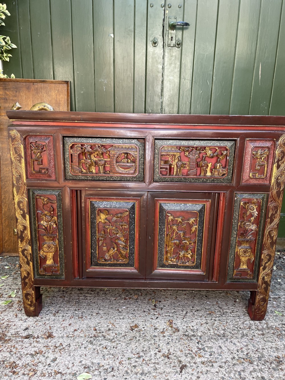 A late nineteenth-century Chinese Qing Dynasty red lacquered side cabinet featuring relief-carved gilded wood panels depicted with architectural scenes, figures, and foliage. View III