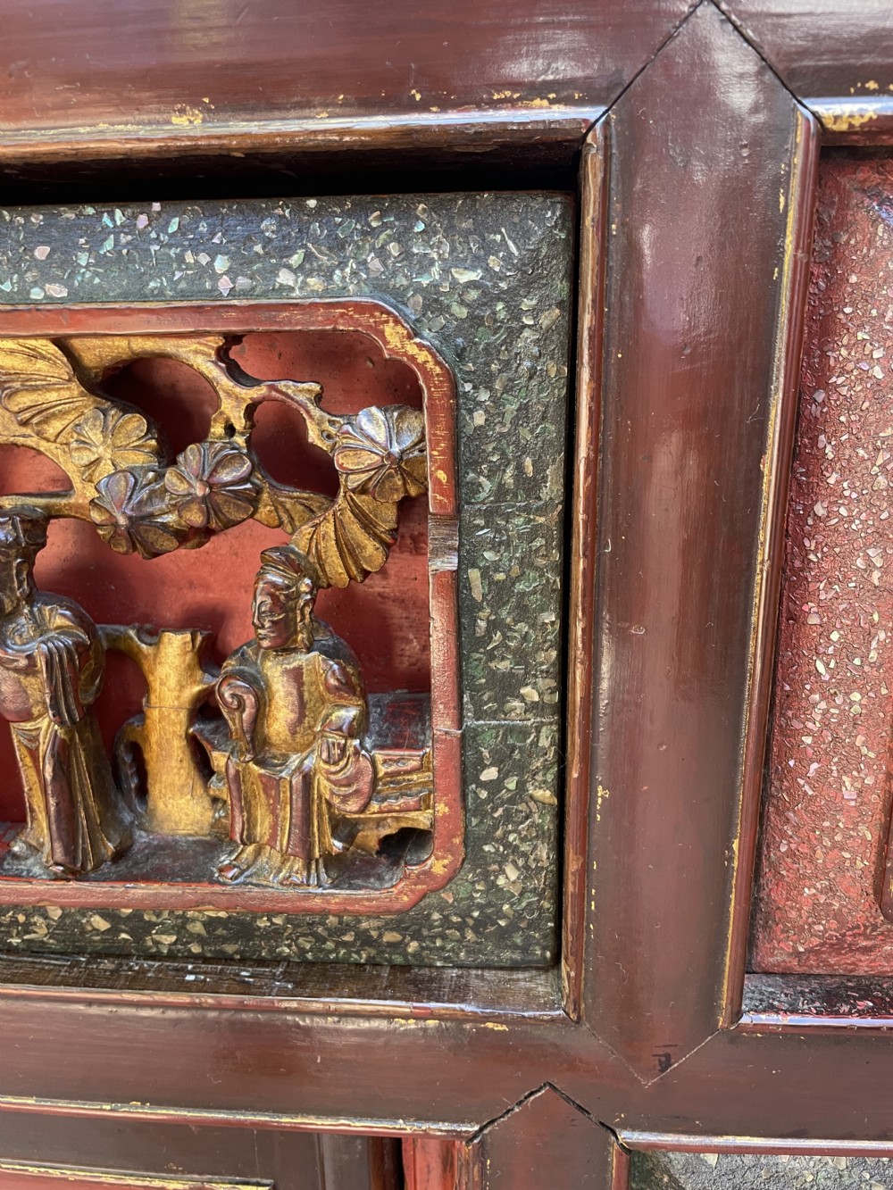 A late nineteenth-century Chinese Qing Dynasty red lacquered side cabinet featuring relief-carved gilded wood panels depicted with architectural scenes, figures, and foliage. View VI