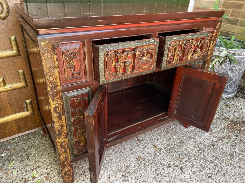 A late nineteenth-century Chinese Qing Dynasty red lacquered side cabinet featuring relief-carved gilded wood panels depicted with architectural scenes, figures, and foliage. View IX