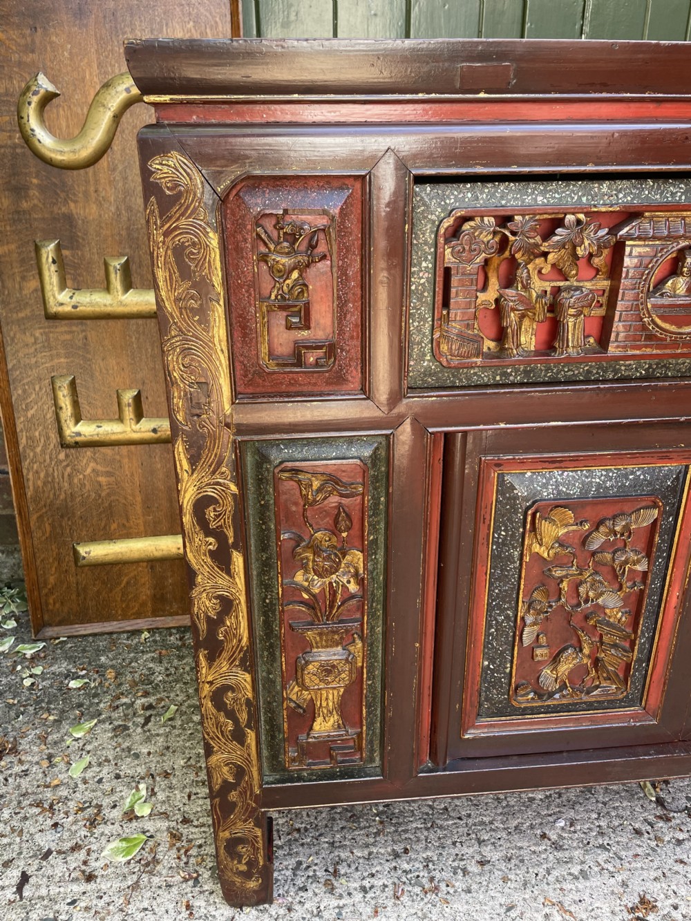 A late nineteenth-century Chinese Qing Dynasty red lacquered side cabinet featuring relief-carved gilded wood panels depicted with architectural scenes, figures, and foliage. View X