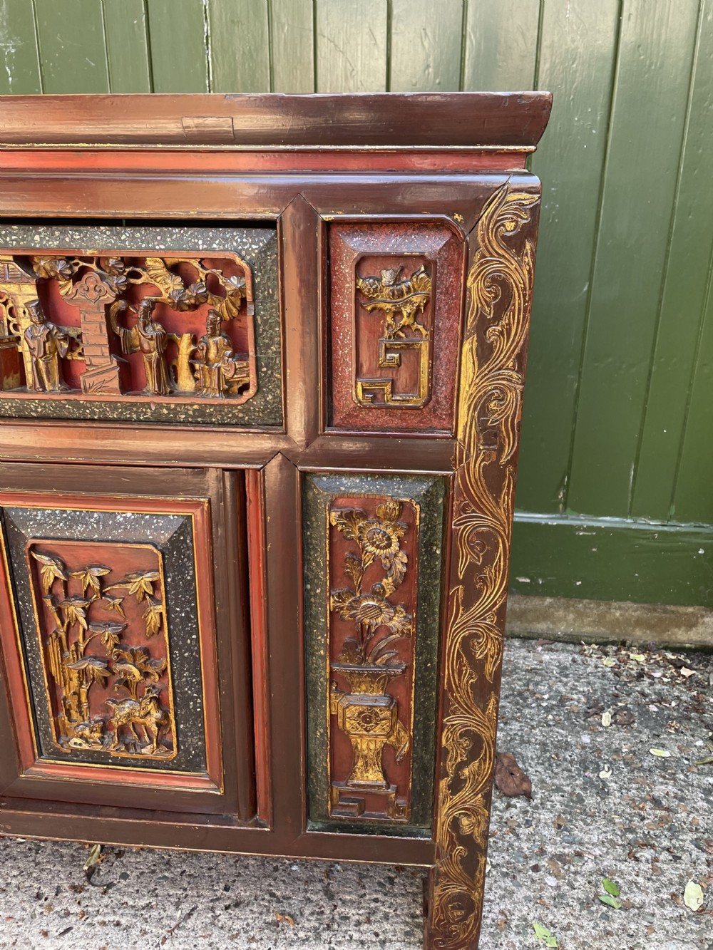 A late nineteenth-century Chinese Qing Dynasty red lacquered side cabinet featuring relief-carved gilded wood panels depicted with architectural scenes, figures, and foliage. View XI