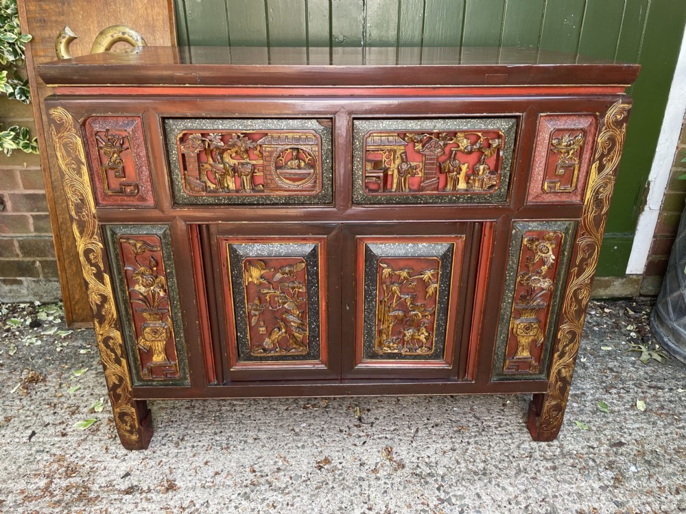 A late nineteenth-century Chinese Qing Dynasty red lacquered side cabinet featuring relief-carved gilded wood panels depicted with architectural scenes, figures, and foliage. View XII