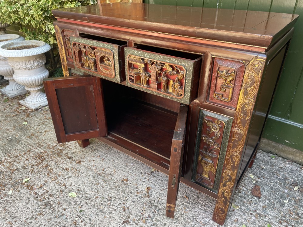 A late nineteenth-century Chinese Qing Dynasty red lacquered side cabinet featuring relief-carved gilded wood panels depicted with architectural scenes, figures, and foliage. View XVI