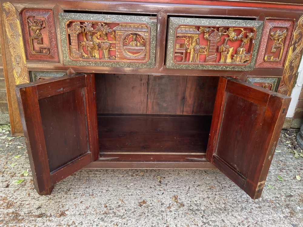 A late nineteenth-century Chinese Qing Dynasty red lacquered side cabinet featuring relief-carved gilded wood panels depicted with architectural scenes, figures, and foliage. View XVII