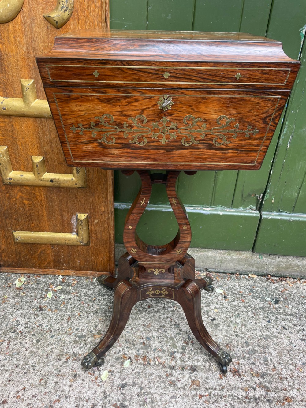 An early 19th-century Regency rosewood teapoy featuring floral brass inlay, a lyre-shaped stem support, and quadruped splayed legs with brass claw feet.