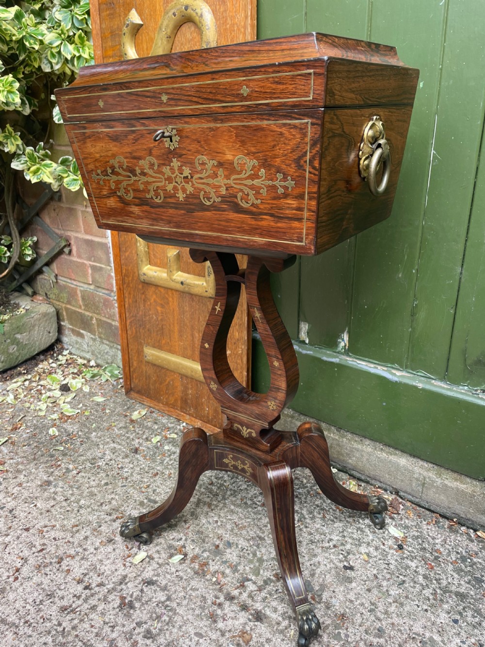 An early 19th-century Regency rosewood teapoy featuring floral brass inlay, a lyre-shaped stem support, and quadruped splayed legs with brass claw feet. View V