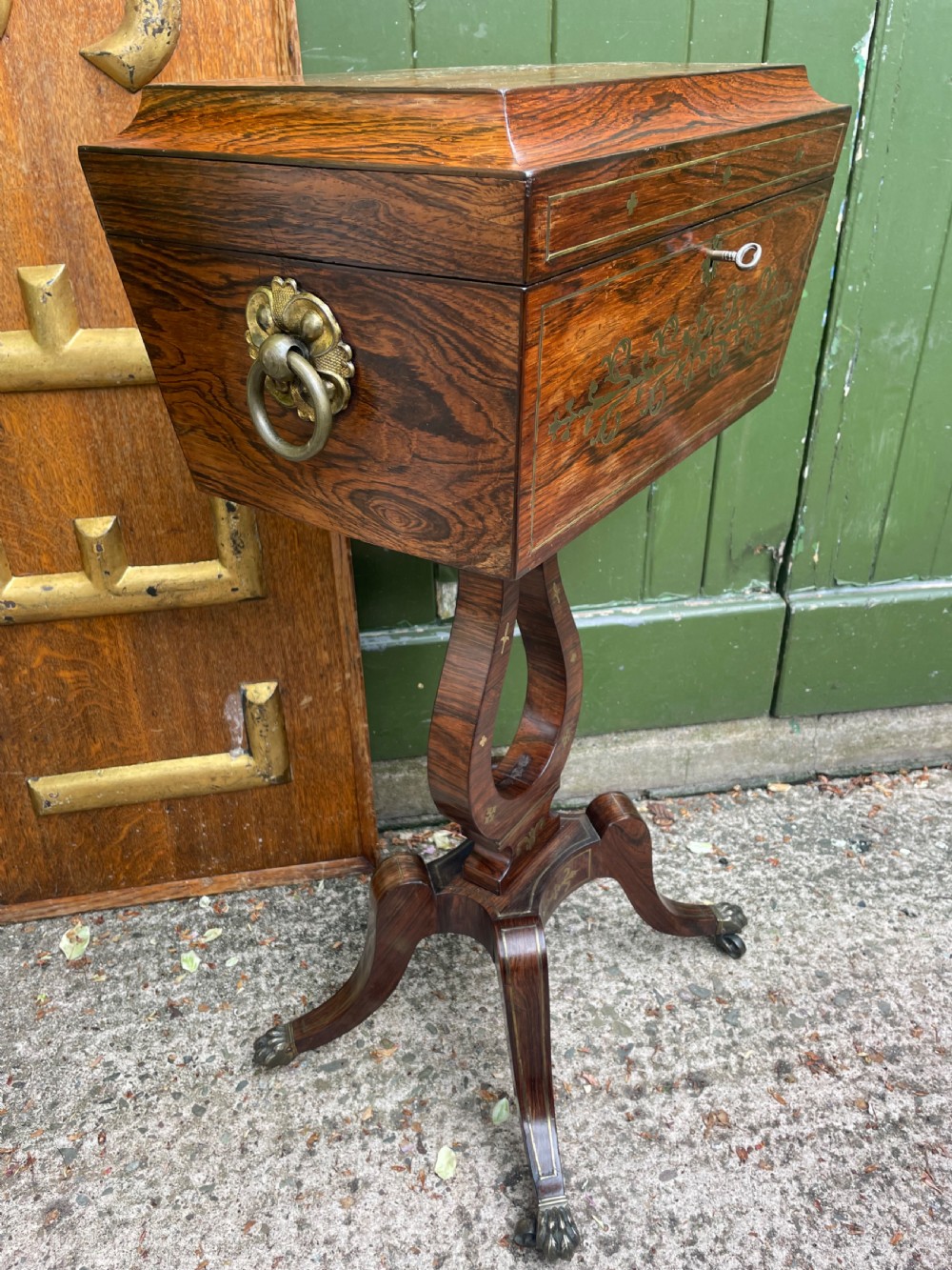 An early 19th-century Regency rosewood teapoy featuring floral brass inlay, a lyre-shaped stem support, and quadruped splayed legs with brass claw feet. View XV