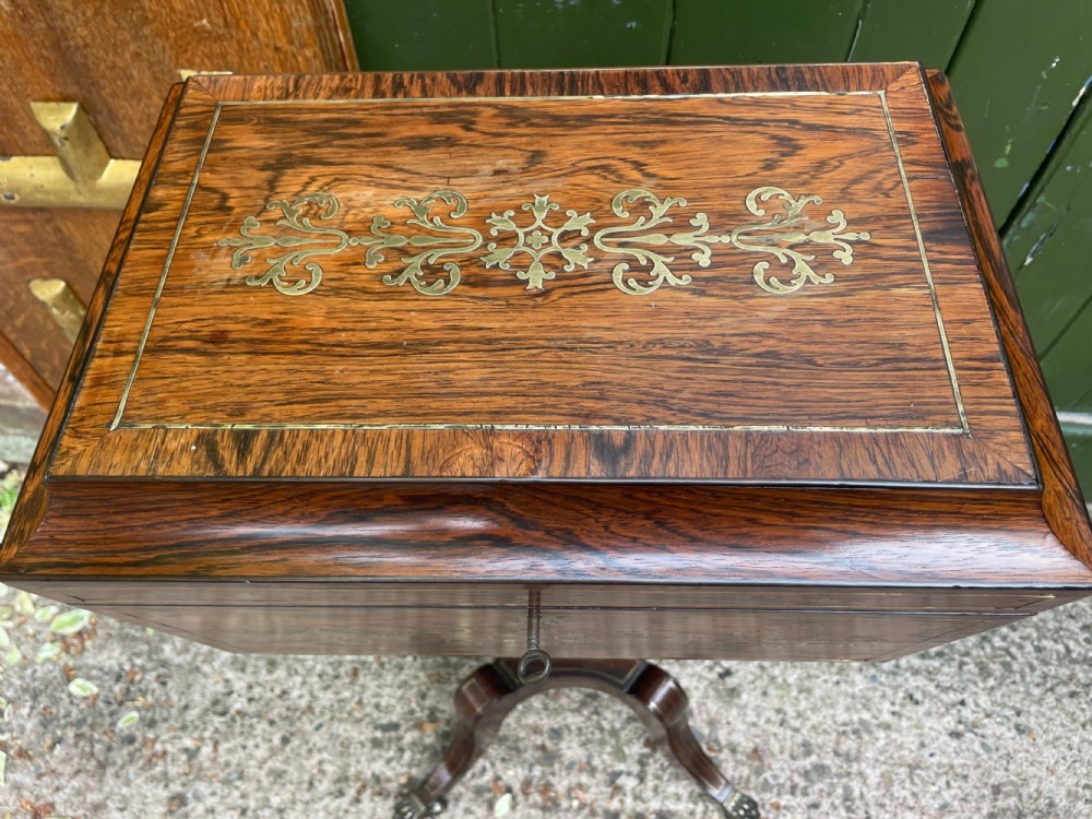 An early 19th-century Regency rosewood teapoy featuring floral brass inlay, a lyre-shaped stem support, and quadruped splayed legs with brass claw feet. View VI