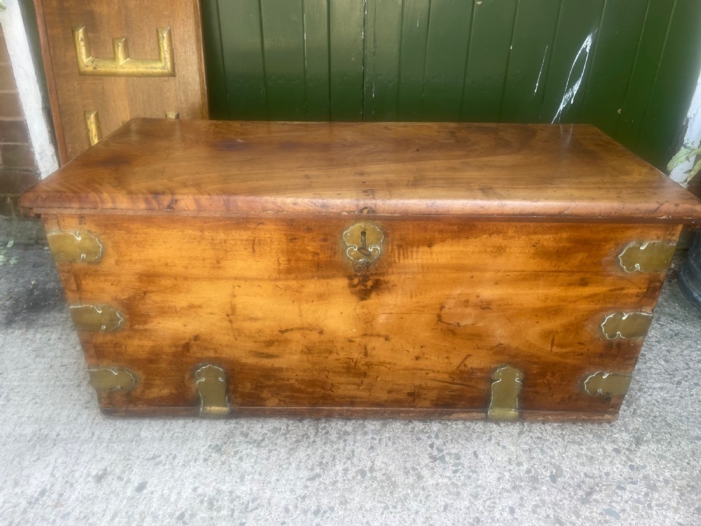 A mid-eighteenth century solid cedar trunk featuring decorative brass corner brackets, brass straps, and a central brass keyhole escutcheon.
