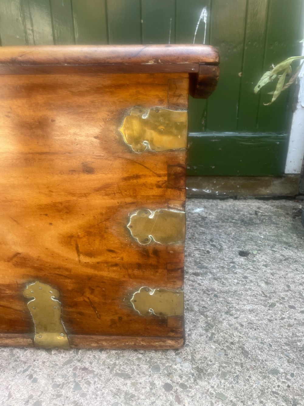 A mid-eighteenth century solid cedar trunk featuring decorative brass corner brackets, brass straps, and a central brass keyhole escutcheon. View II
