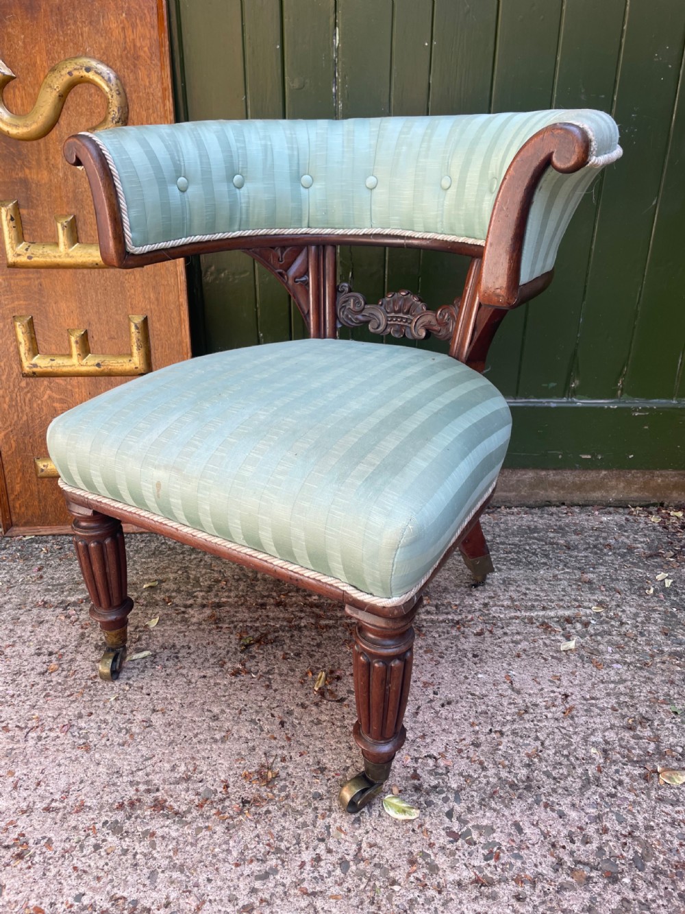 A George IV mahogany curule library armchair upholstered in pale green striped buttoned fabric with reeded front legs on brass castors.