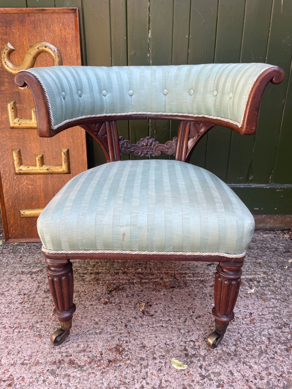 A George IV mahogany curule library armchair upholstered in pale green striped buttoned fabric with reeded front legs on brass castors. View II