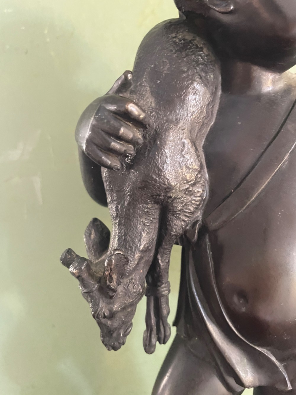 A dark patinated bronze sculpture depicting a standing putto hunter blowing a curved horn while slinging a small deer over one shoulder. View VII