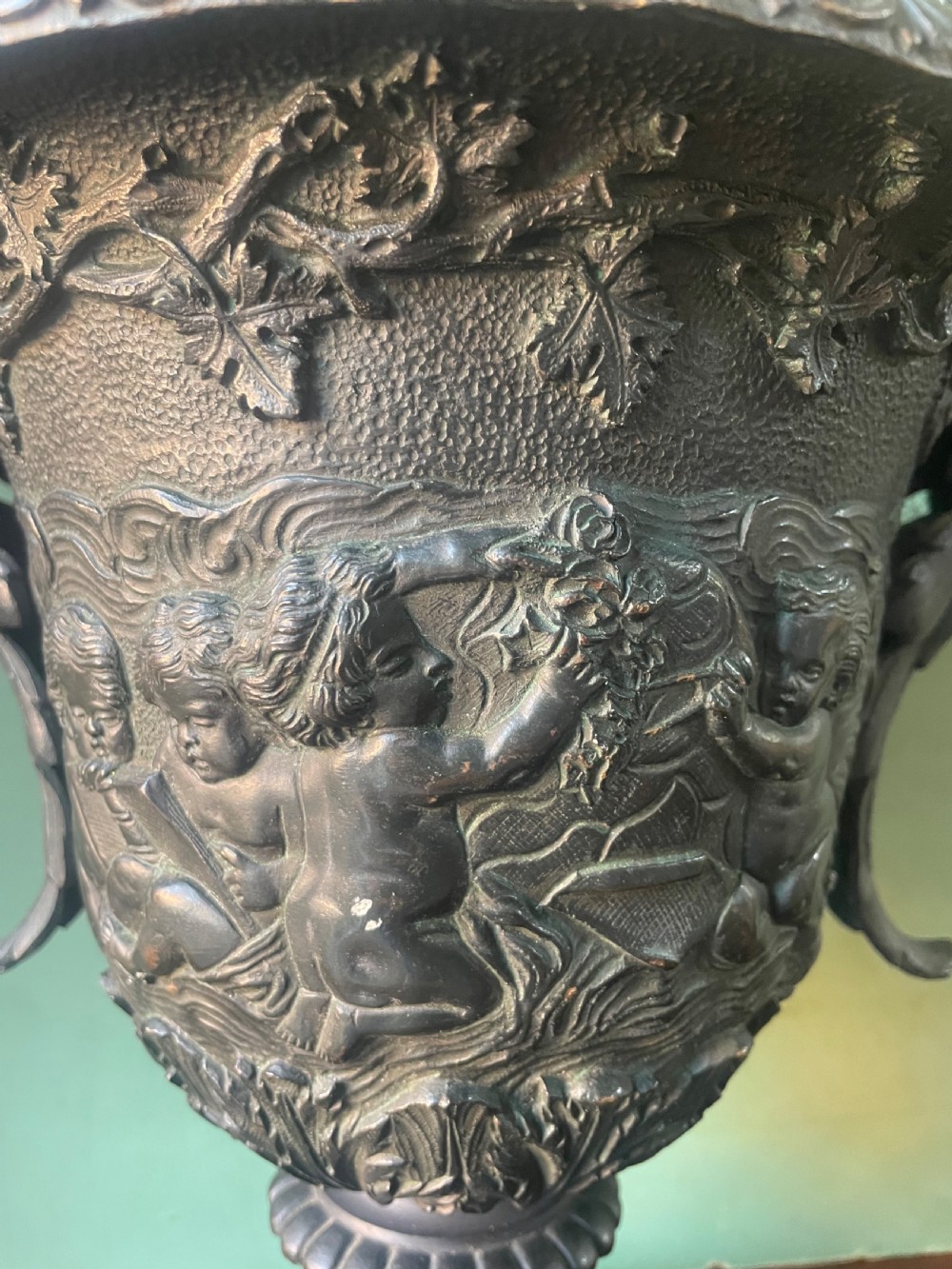 A 19th-century French dark bronze campana-shaped urn featuring relief carving of putti, satyr mask handles, and a square pedestal base. View IX