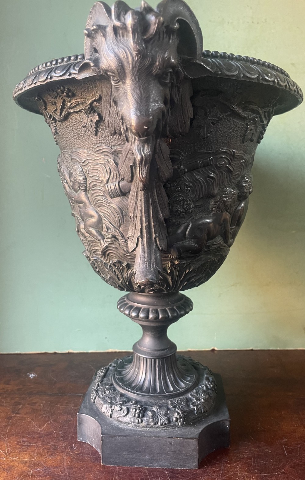 A 19th-century French dark bronze campana-shaped urn featuring relief carving of putti, satyr mask handles, and a square pedestal base. View XIV