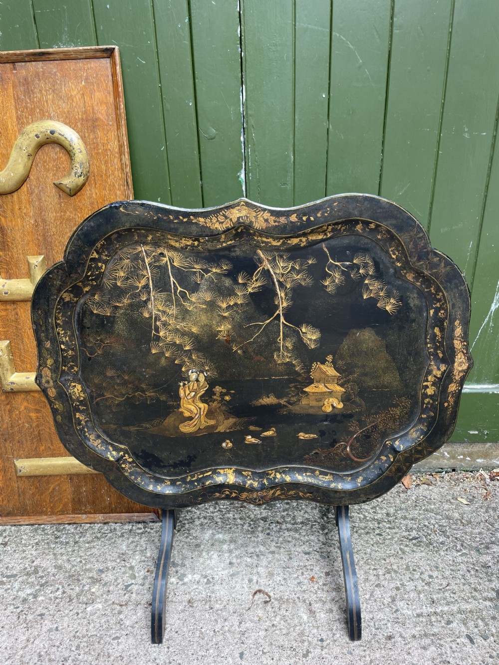 A 19th-century black lacquered papier-mache tray table featuring gilded Chinoiserie landscape decoration and scalloped edges. View XIV