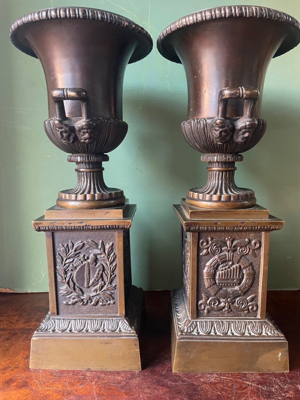 A pair of early 19th-century French Charles X bronze campana-shaped urns with fluted bodies and classical relief motifs on square plinth bases. View II