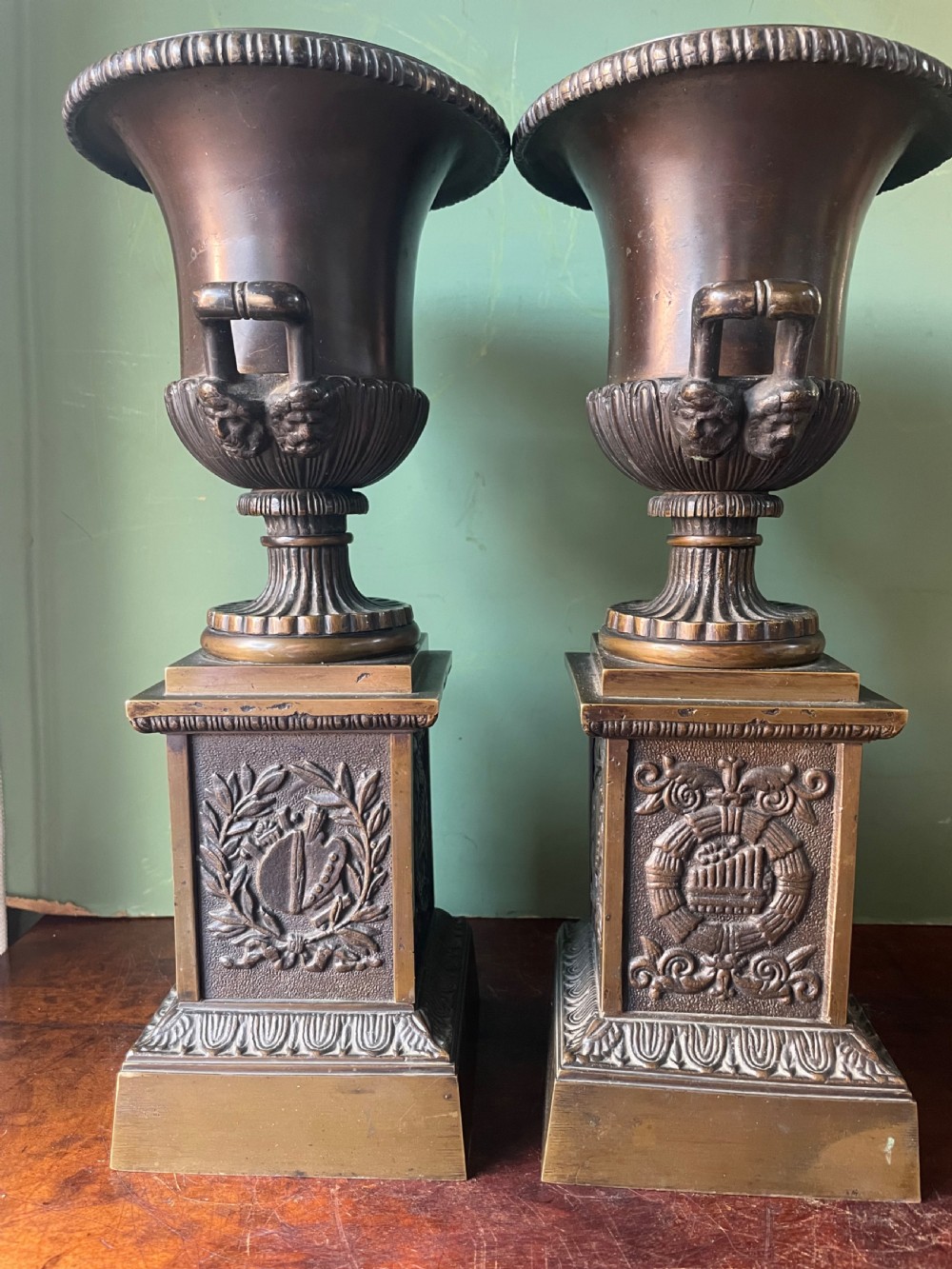 A pair of early 19th-century French Charles X bronze campana-shaped urns with fluted bodies and classical relief motifs on square plinth bases. View V