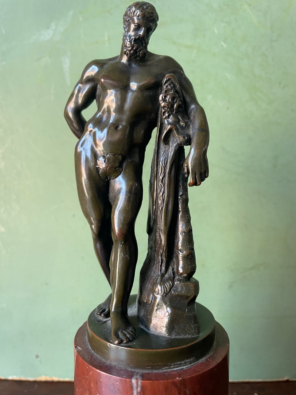 A patinated bronze study of the Farnese Hercules standing against a club draped in lion skin, mounted on a red marble plinth and black base. View III