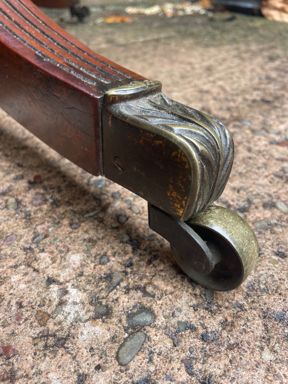 A late George III period circular mahogany tilt-top table shown in a vertical position, featuring a single-piece top and reeded tripod legs with brass castors. View VI