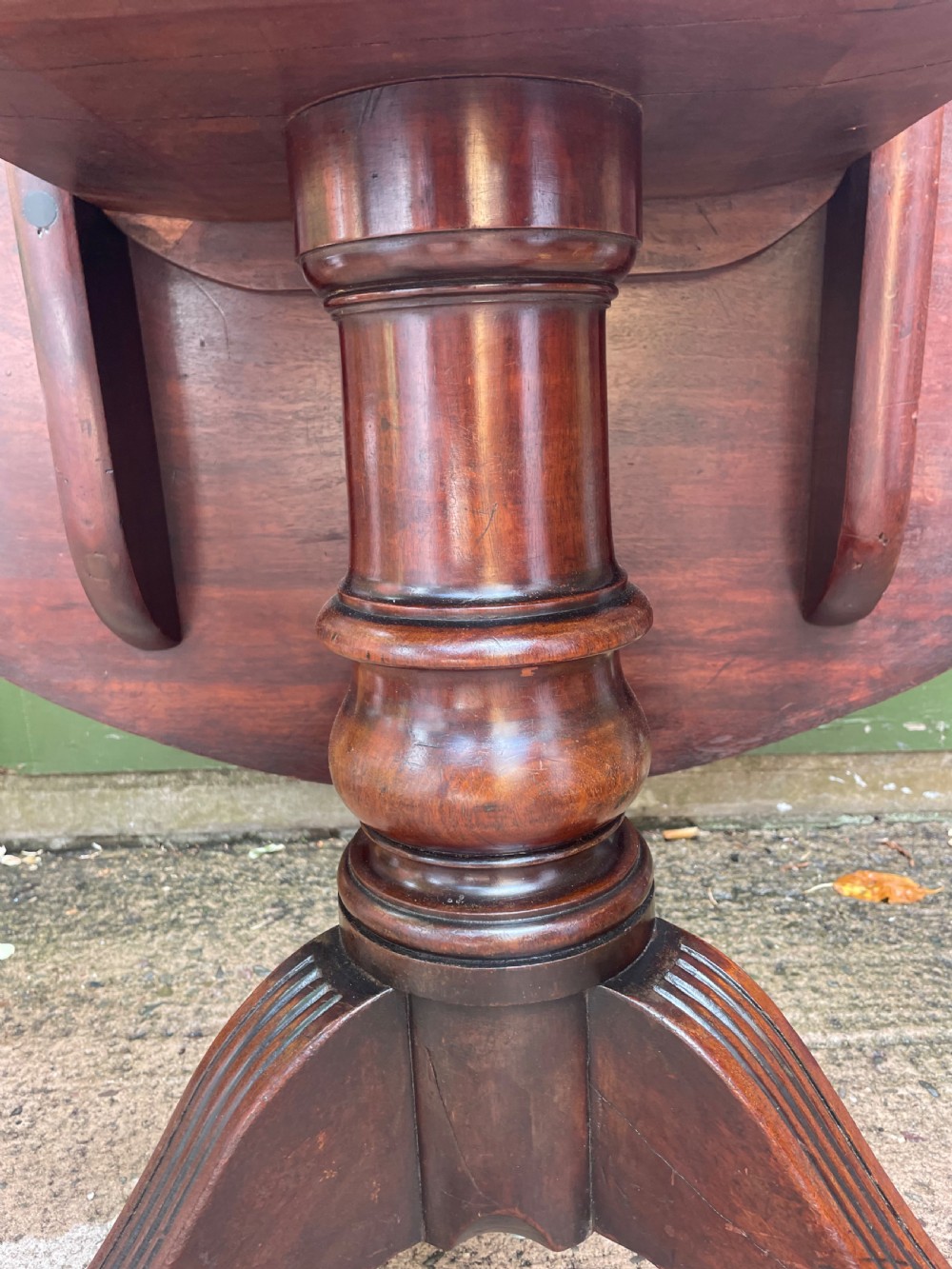 A late George III period circular mahogany tilt-top table shown in a vertical position, featuring a single-piece top and reeded tripod legs with brass castors. View VII