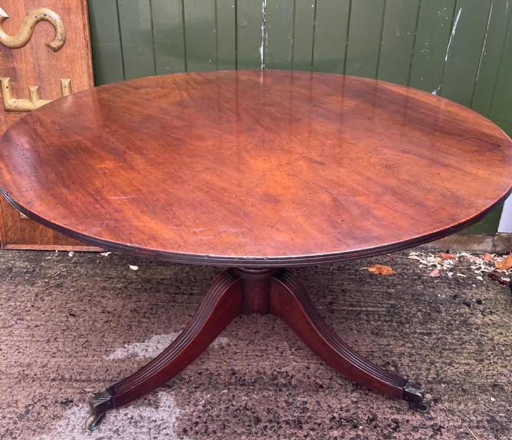 A late George III period circular mahogany tilt-top table shown in a vertical position, featuring a single-piece top and reeded tripod legs with brass castors. View XIII