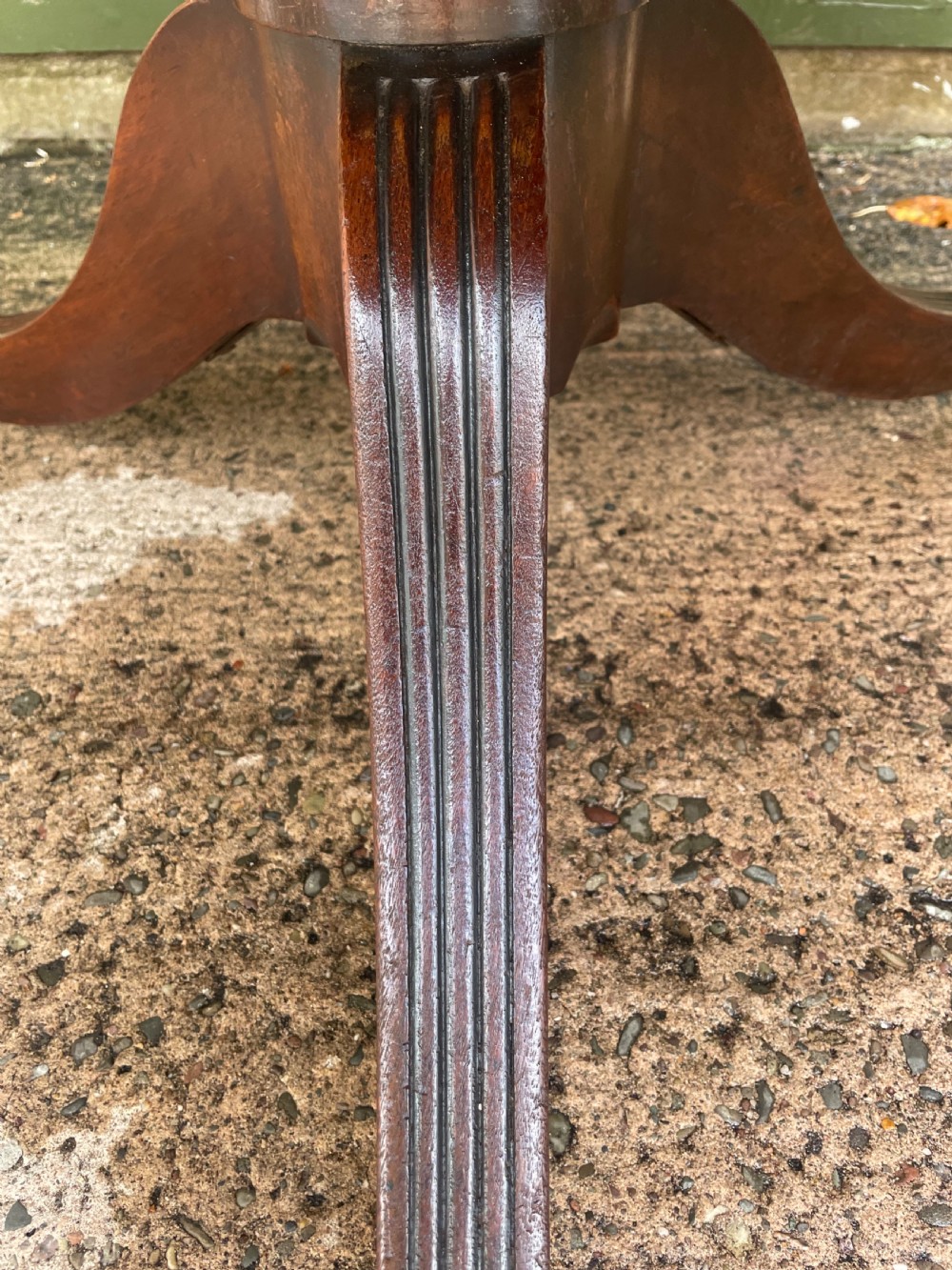 A late George III period circular mahogany tilt-top table shown in a vertical position, featuring a single-piece top and reeded tripod legs with brass castors. View XX