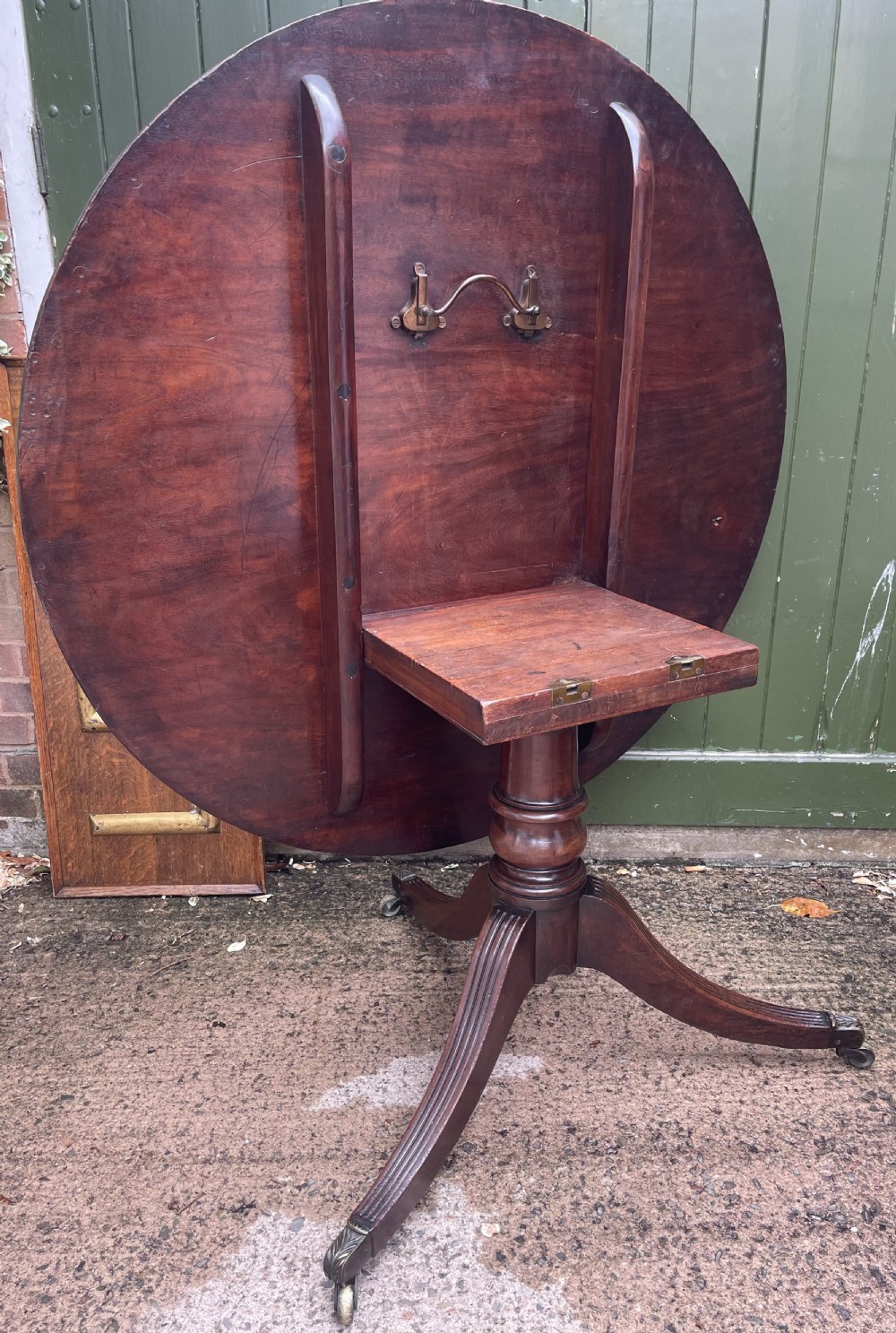 A late George III period circular mahogany tilt-top table shown in a vertical position, featuring a single-piece top and reeded tripod legs with brass castors. View XXVI
