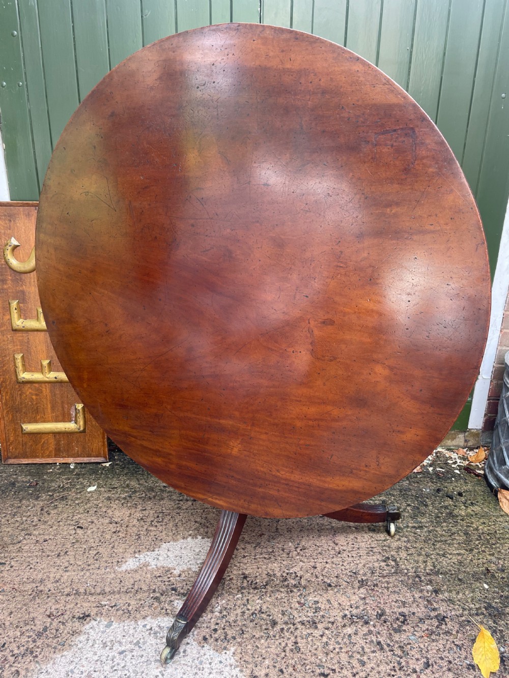 A late George III period circular mahogany tilt-top table shown in a vertical position, featuring a single-piece top and reeded tripod legs with brass castors. View XXVII