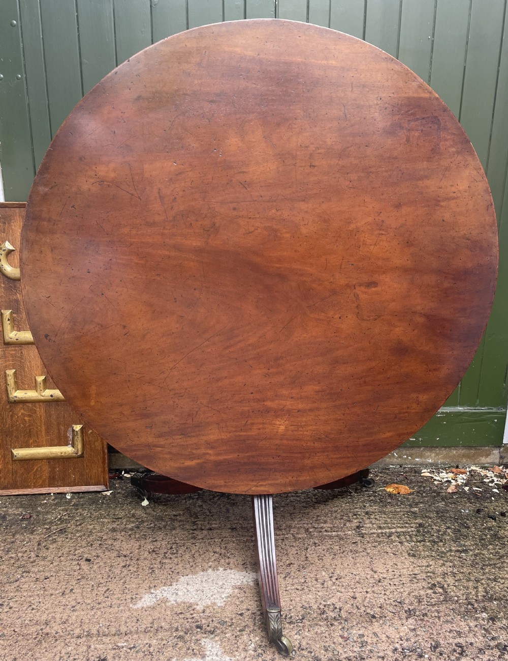 A late George III period circular mahogany tilt-top table shown in a vertical position, featuring a single-piece top and reeded tripod legs with brass castors. View XXIX