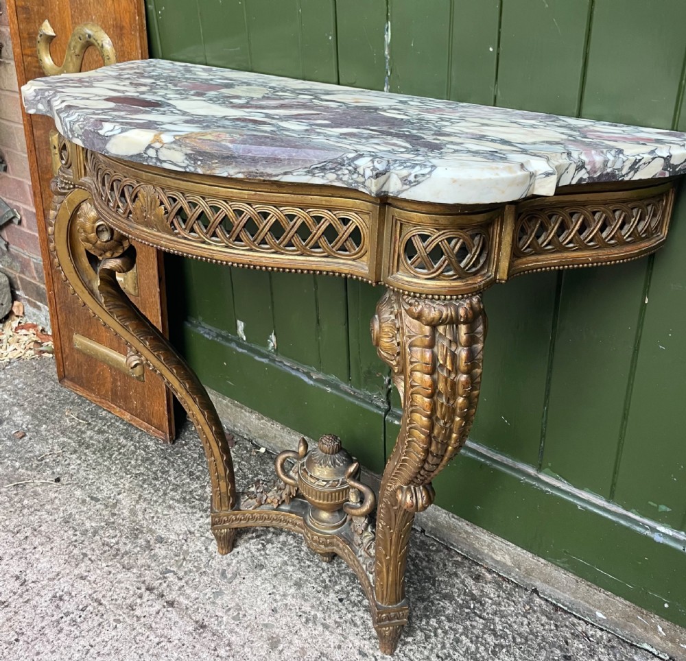 A 19th-century French giltwood console table featuring a serpentine variegated marble top, pierced lattice frieze, and carved urn stretcher. View II