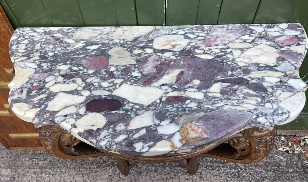 A 19th-century French giltwood console table featuring a serpentine variegated marble top, pierced lattice frieze, and carved urn stretcher. View V