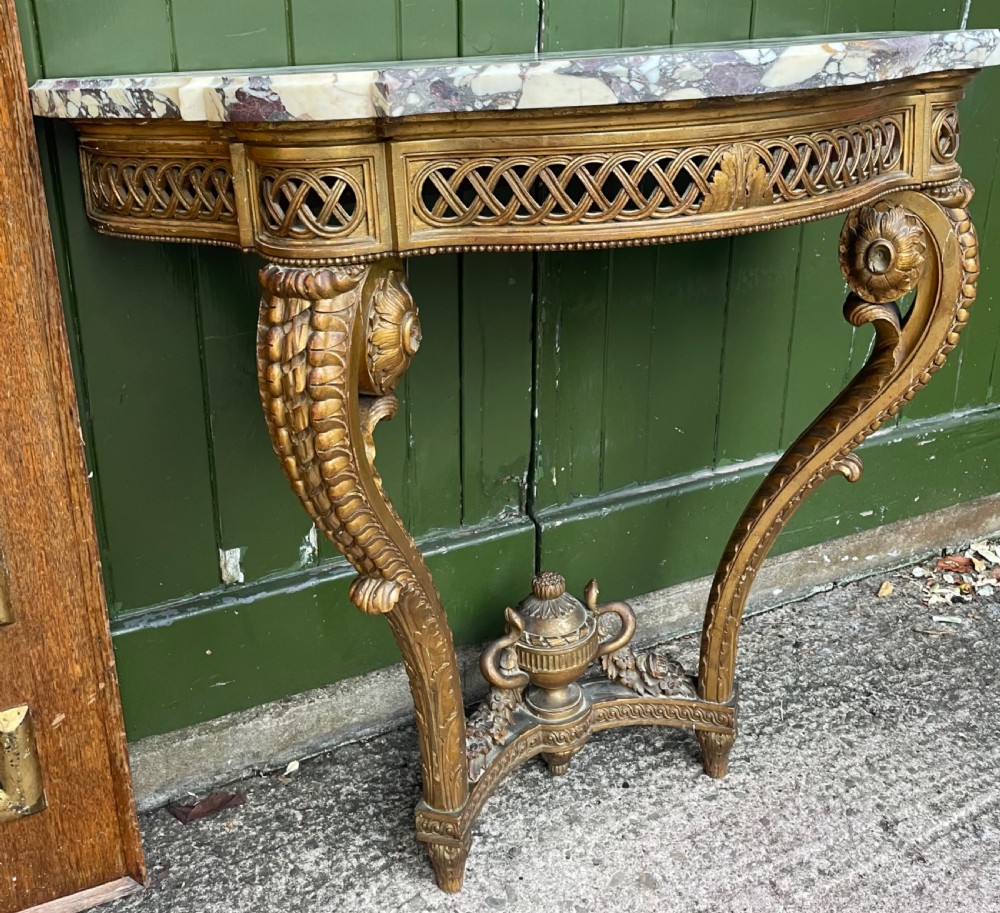 A 19th-century French giltwood console table featuring a serpentine variegated marble top, pierced lattice frieze, and carved urn stretcher. View VII
