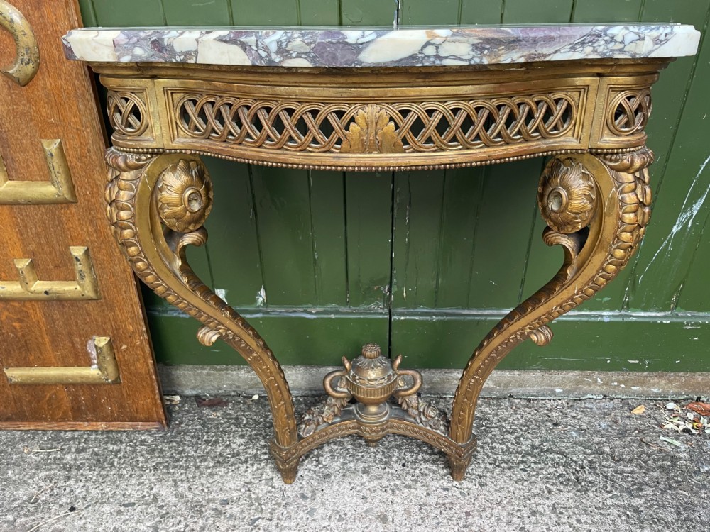 A 19th-century French giltwood console table featuring a serpentine variegated marble top, pierced lattice frieze, and carved urn stretcher. View VIII