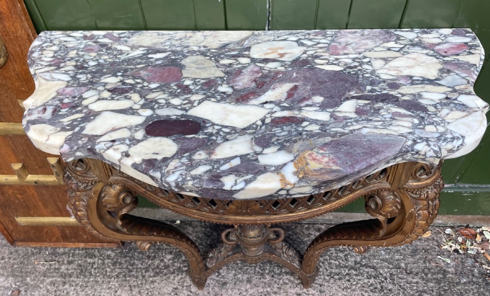 A 19th-century French giltwood console table featuring a serpentine variegated marble top, pierced lattice frieze, and carved urn stretcher. View IX