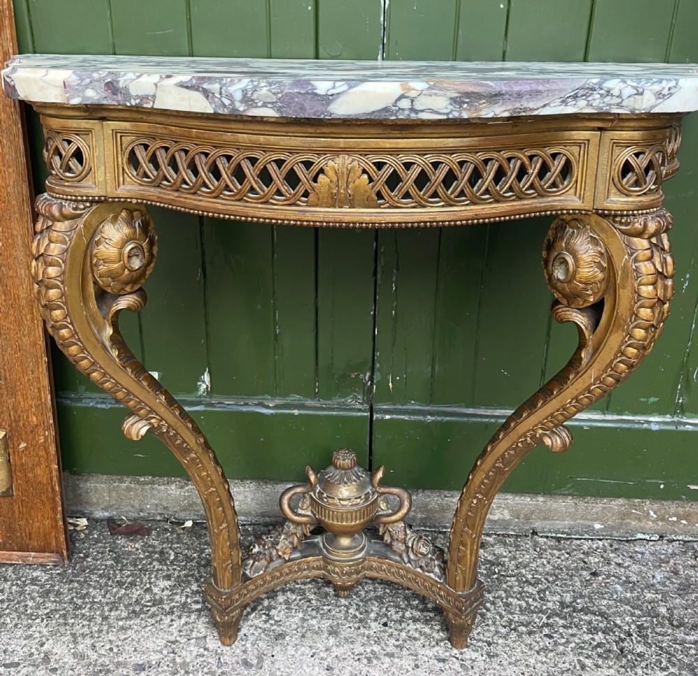 A 19th-century French giltwood console table featuring a serpentine variegated marble top, pierced lattice frieze, and carved urn stretcher. View X
