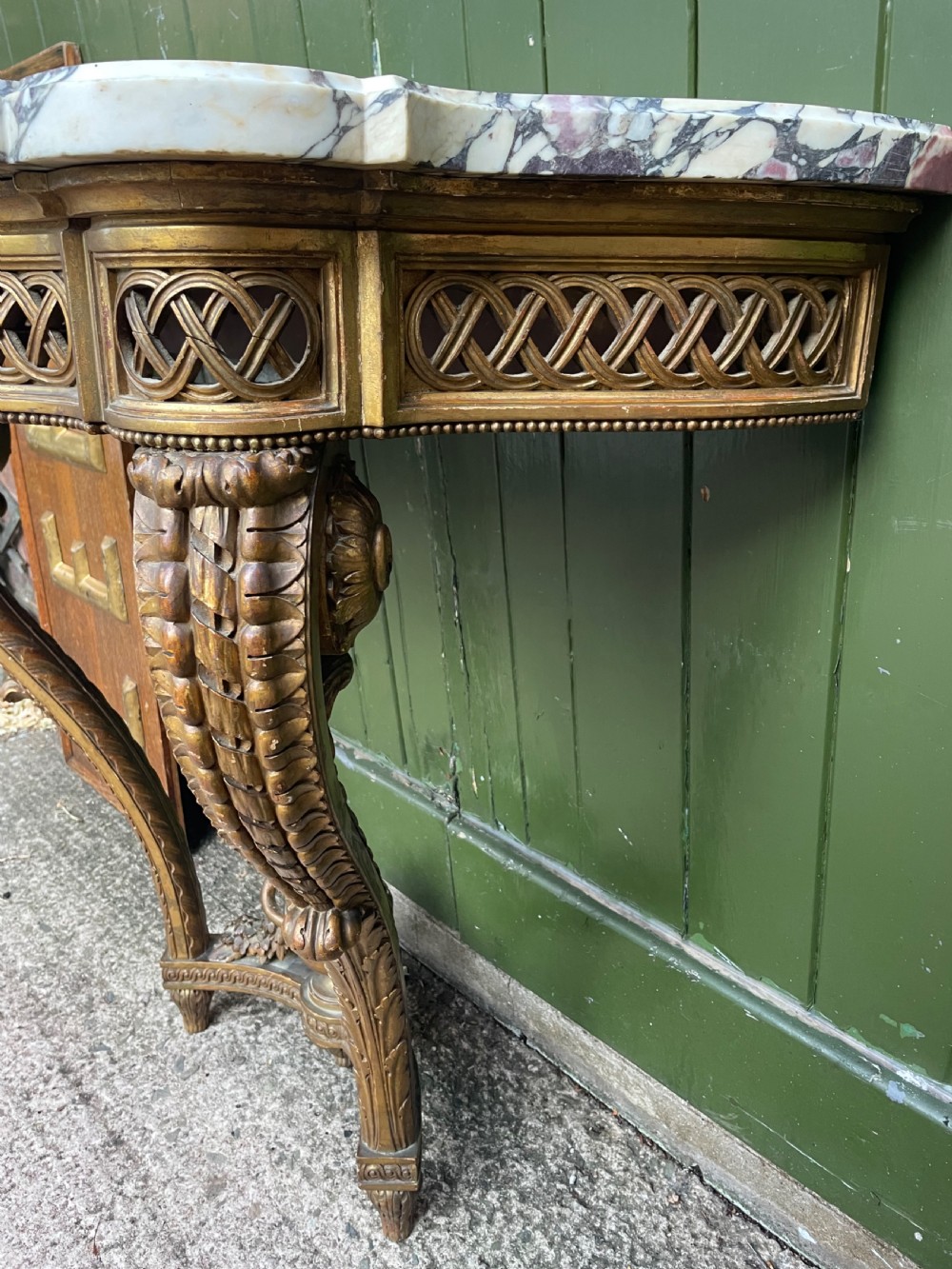A 19th-century French giltwood console table featuring a serpentine variegated marble top, pierced lattice frieze, and carved urn stretcher. View XIII