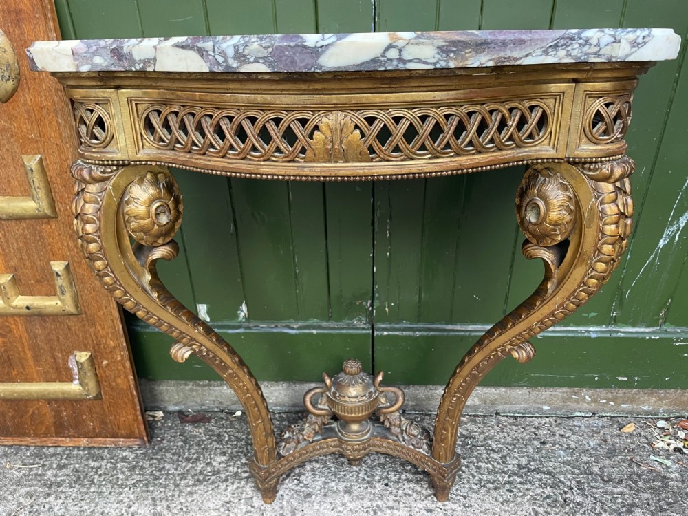 A 19th-century French giltwood console table featuring a serpentine variegated marble top, pierced lattice frieze, and carved urn stretcher. View XVI