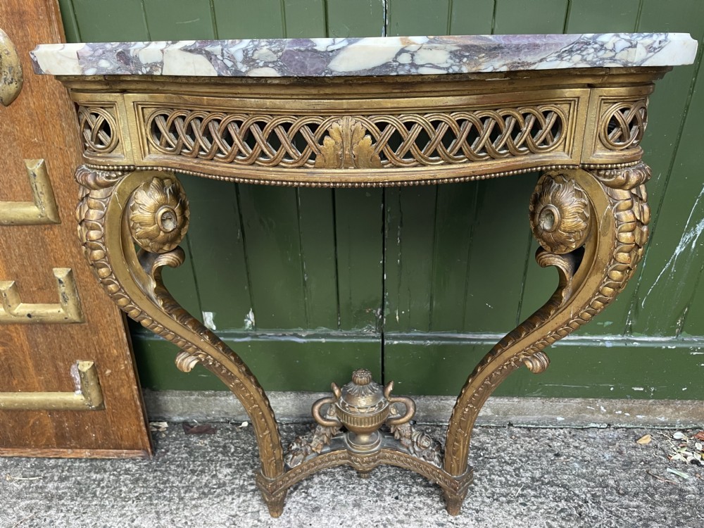 A 19th-century French giltwood console table featuring a serpentine variegated marble top, pierced lattice frieze, and carved urn stretcher. View XXII