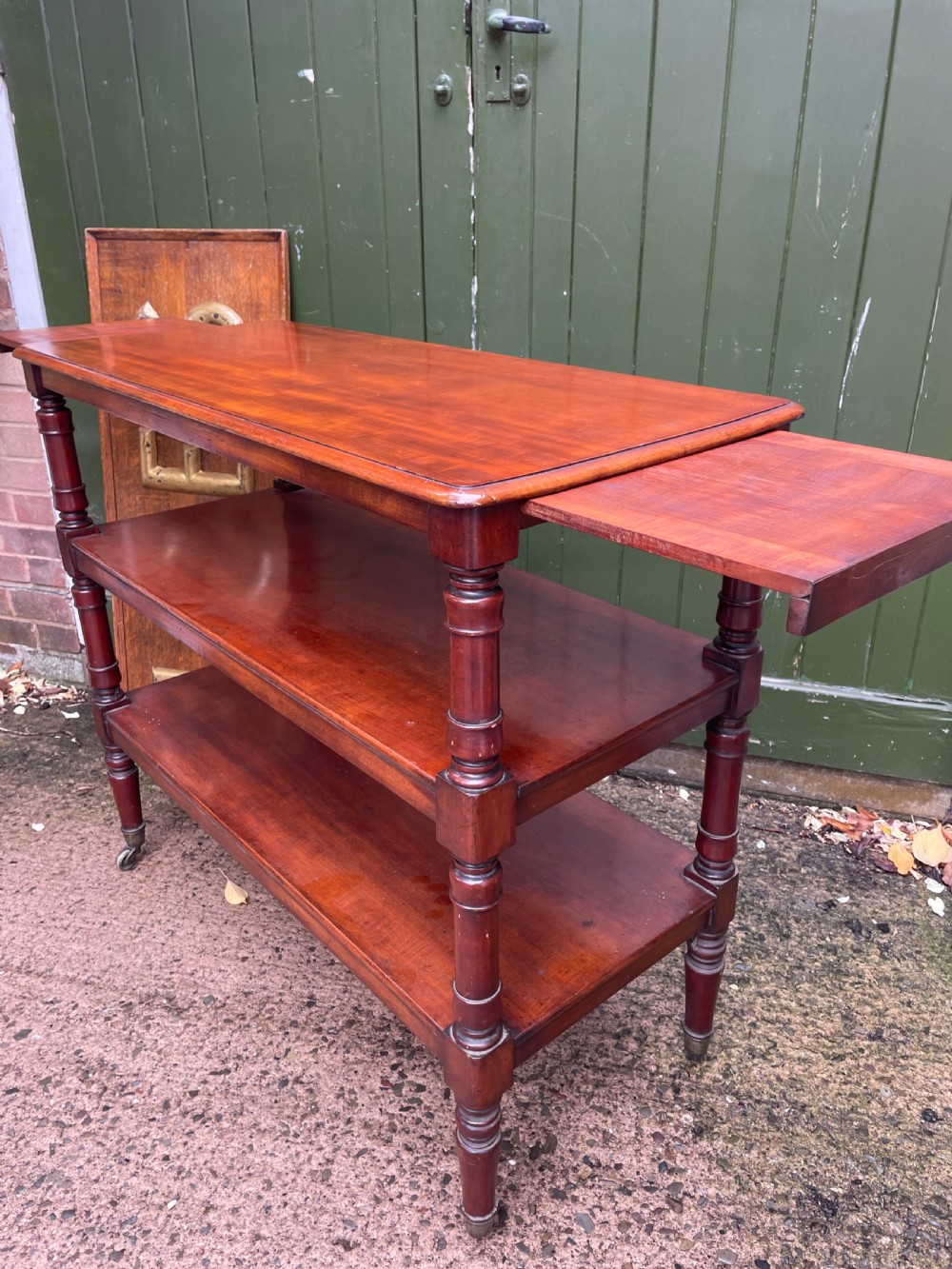 A three-tier George IV mahogany buffet table featuring turned column supports and brass castors. View VIII