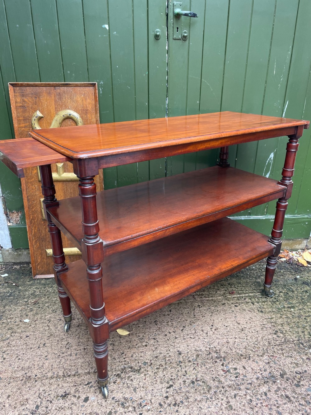 A three-tier George IV mahogany buffet table featuring turned column supports and brass castors. View XIII