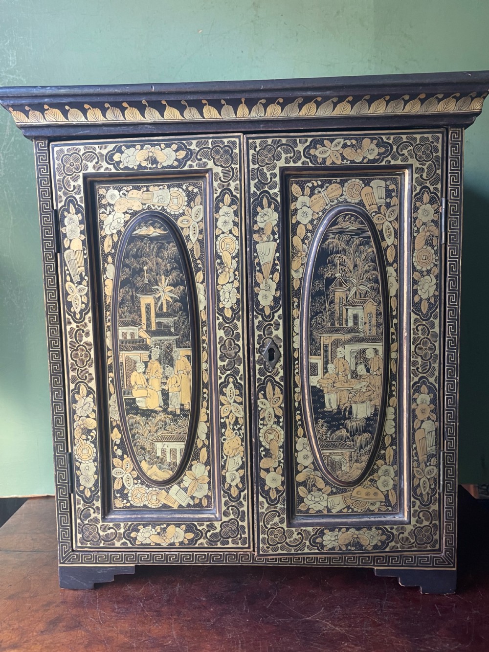 A mid-nineteenth century Chinese export black lacquer table cabinet featuring two doors decorated with gilded figural landscapes, floral borders, and geometric motifs. View X