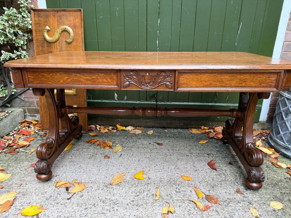 An early 19th-century William IV oak library table featuring a central carved acorn frieze panel, scrolled trestle supports, and a turned stretcher base.